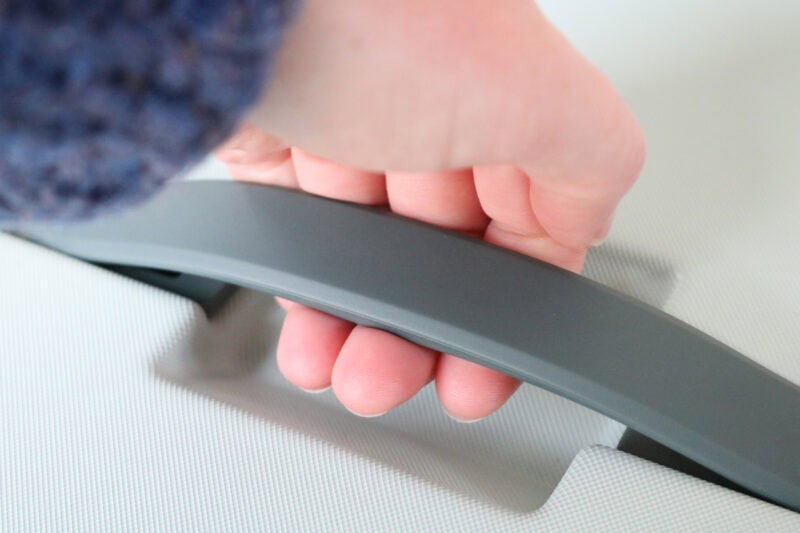 Close-up of a hand gripping the gray handle of a piece of luggage.