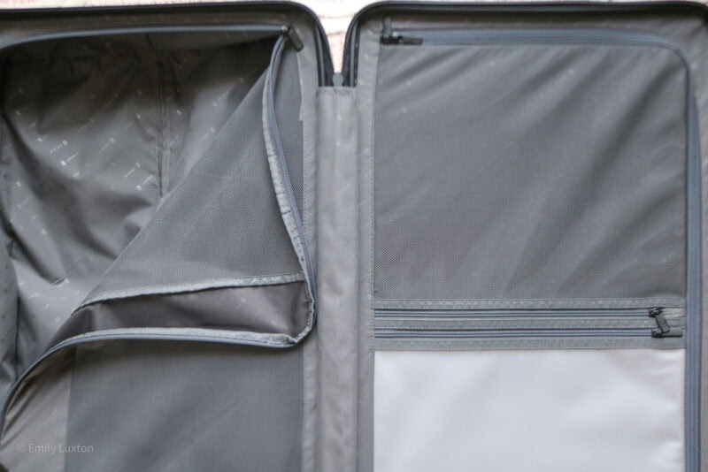 Interior view of an open suitcase with two main compartments, each with mesh dividers. One divider is partially unzipped, revealing the inner lining. The suitcase is empty and well-organized.