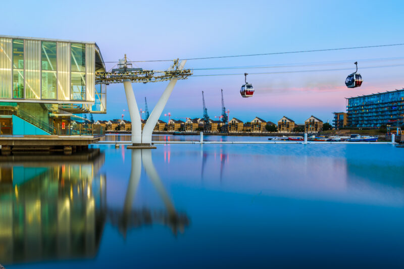 River Thames just after sunset with a pink and blue sky reflected in the calm water and two cable cars passing overehad