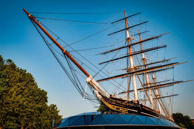 Old wooden tallship with two tall masts and a long wooden bowsprit against a blue sky