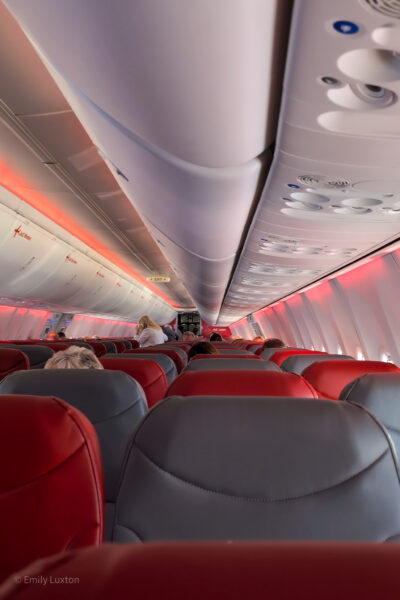 Airplane cabin with red and gray seats, passengers seated, closed overhead compartments, and warm lighting from the ceiling. Jet2 holidays flight to Tenerife review.