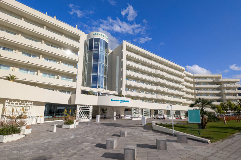 Modern hotel 'Iberostar Selection Sábila' with multiple floors, balconies, and a glass elevator shaft, under a sunny sky.