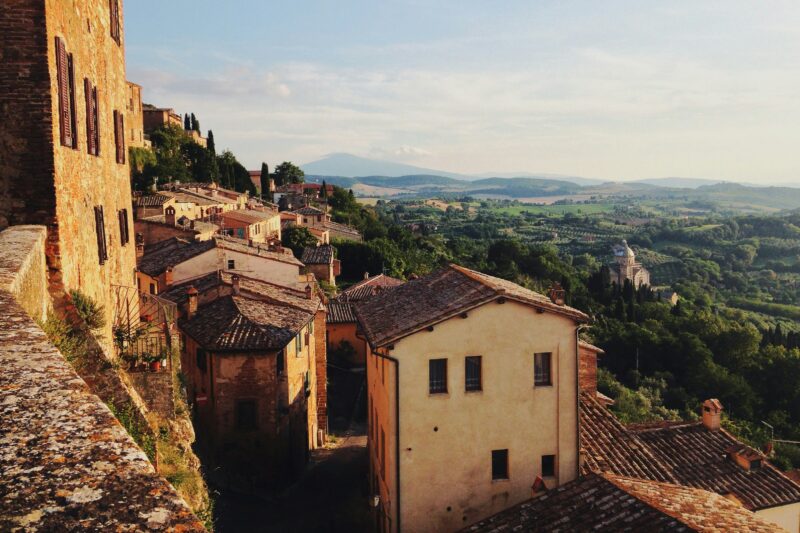 brown stone houses on the edge of a hill around sunset with a view of tuscan countryside below