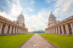 Stone path across a lawn framed by two white collonaded buildings with two small domed-roof towers at the end