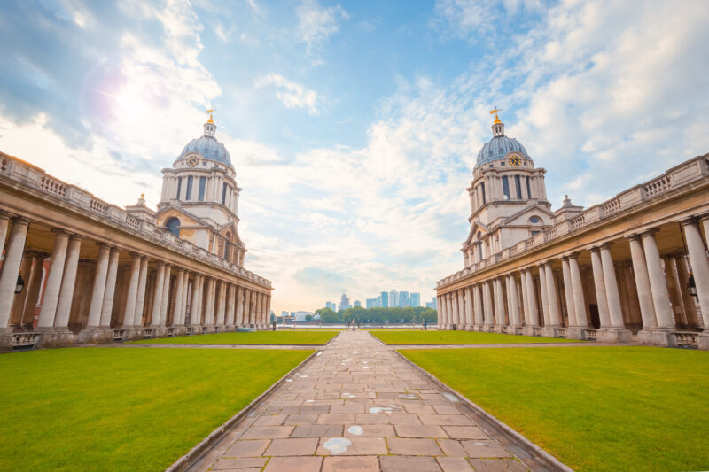 Stone path across a lawn framed by two white collonaded buildings with two small domed-roof towers at the end